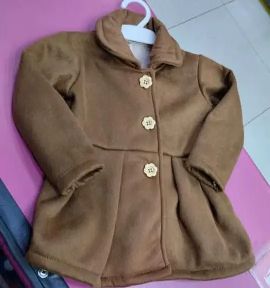 Abrigo de niña color camello con botones de madera y cuello alto, diseño elegante y abrigador.